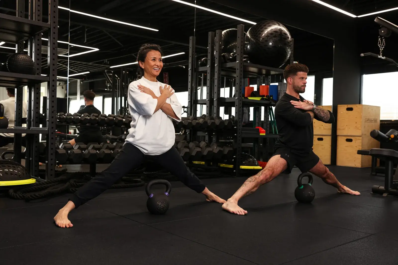 Trainer en klant zakken lachend naast elkaar door in een zijwaartse uitval met kettlebells