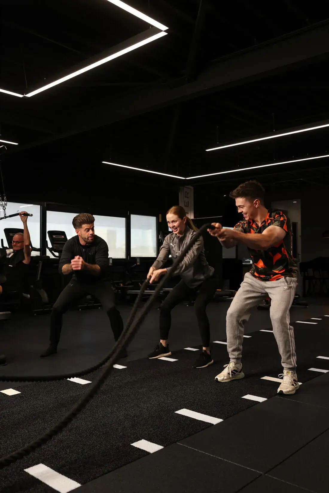 Twee klanten trainen samen met battle ropes onder begeleiding van hun trainer