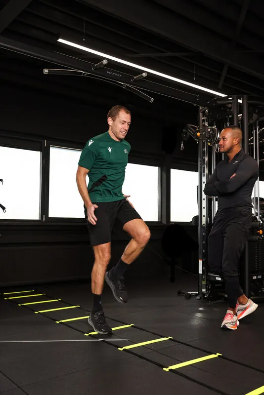 Klant traint voetenwerk op de loopladder terwijl de trainer meekijkt