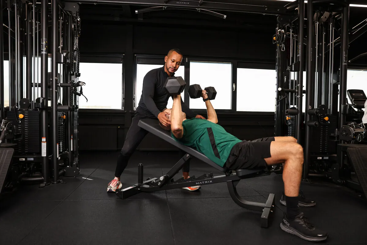 Trainer geeft rugdekking bij het drukken met dumbbells op de schuine bank