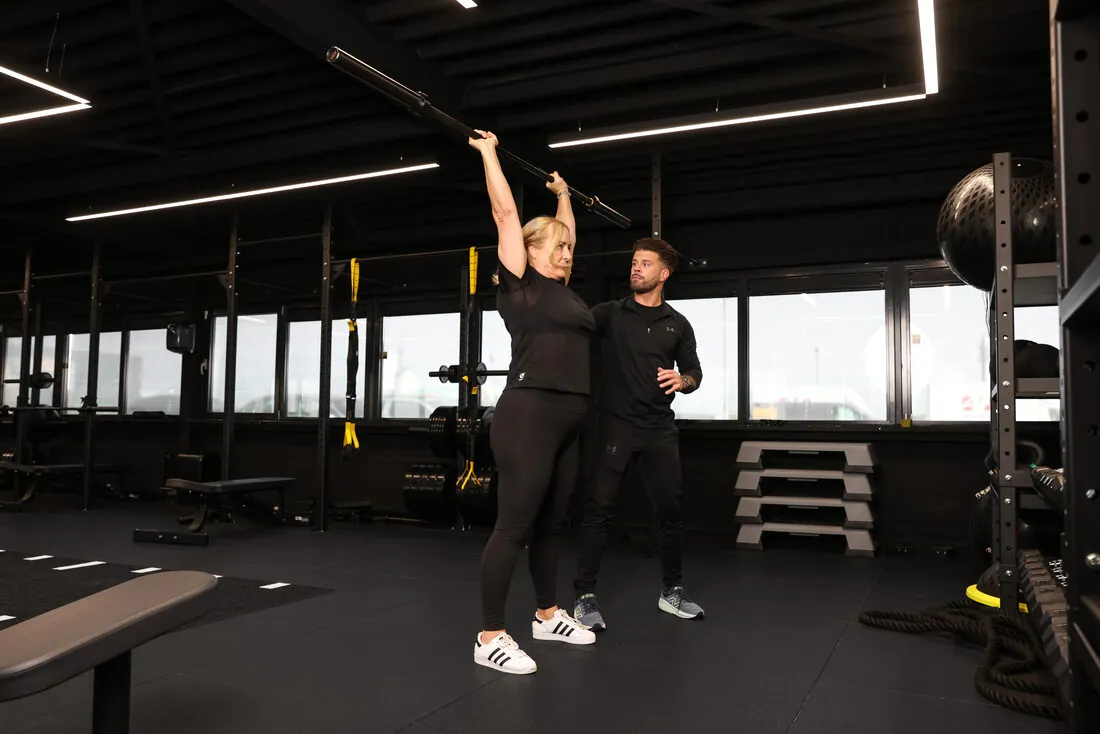 Trainer begeleidt een klant bij een oefening met de stang in de gym in Haarlem