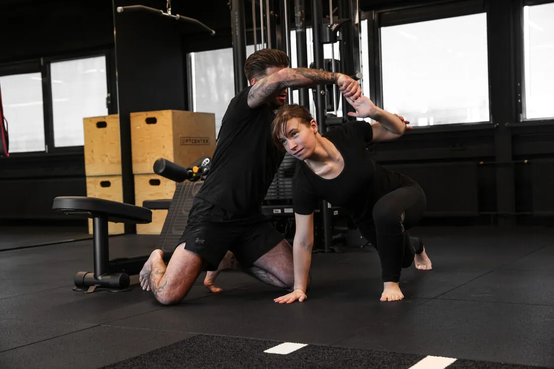 Trainer begeleidt een klant bij een mobility-oefening op de mat