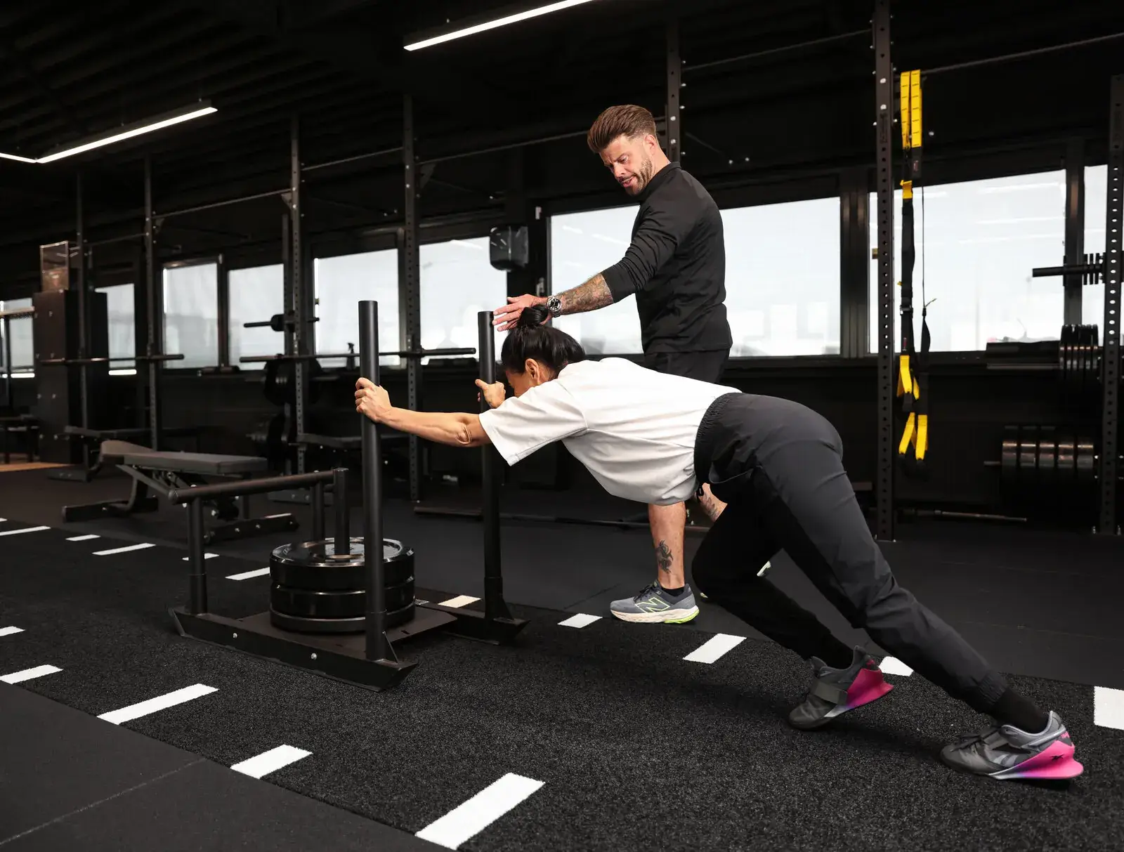 Klant duwt de sled onder begeleiding van een trainer in de gym in Haarlem